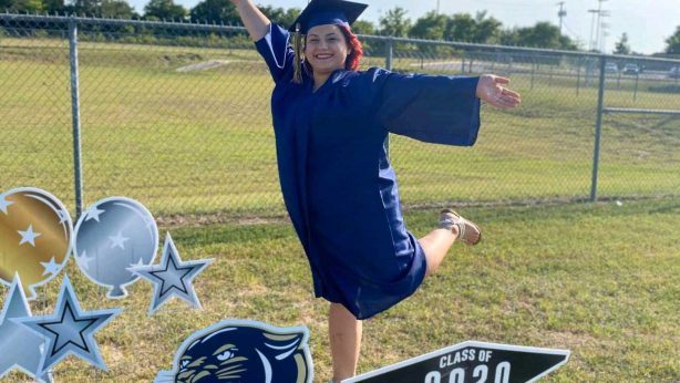 A young lady in graduation gown poses for picture