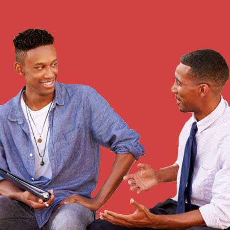 a young man sits and talks with his older male mentor