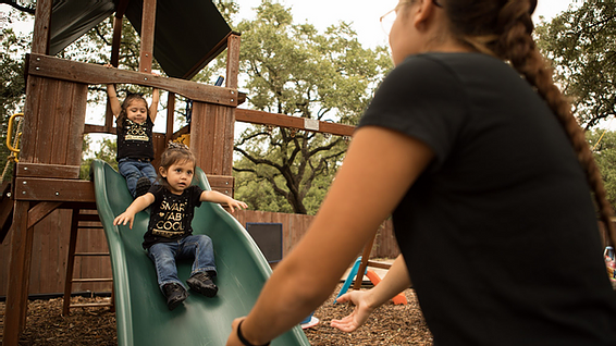 Mother helps her two toddlers slide down jungle gym